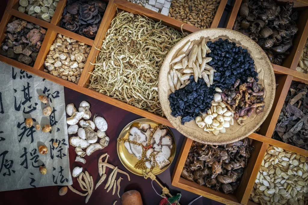 Top-down view of dried herbs, a brass scale, and calligraphy on a wooden cabinet.