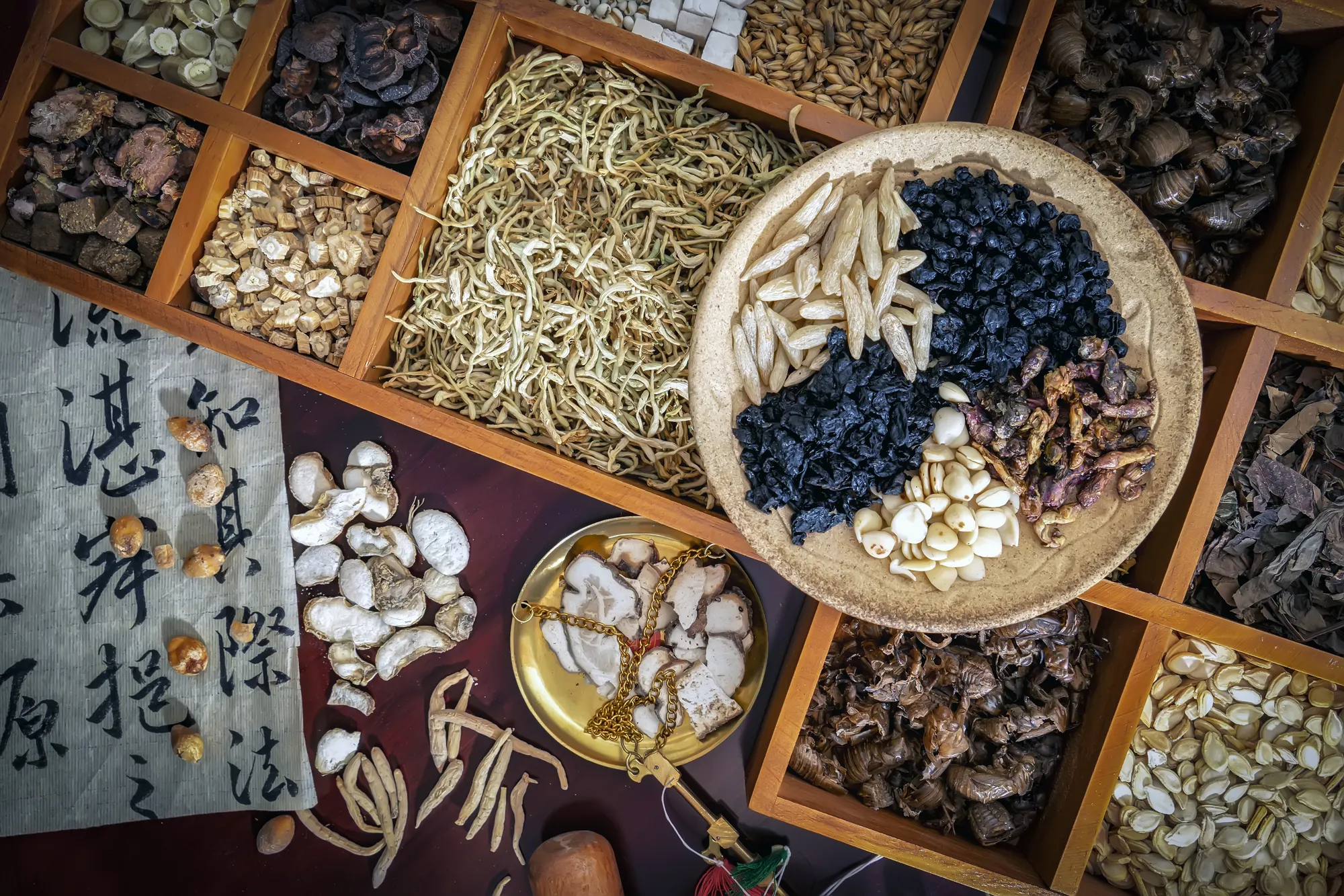 Top-down view of dried herbs, a brass scale, and calligraphy on a wooden cabinet.