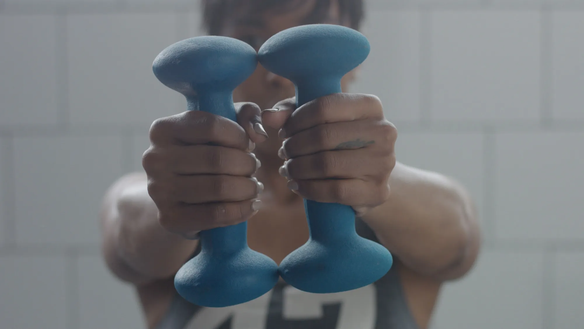Front shot focusing on hands holding two blue dumbbells together at chest height.