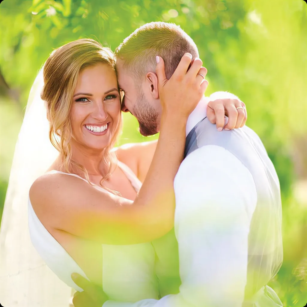 A close-up of Jemma smiling while hugging her groom in a sunlit garden.