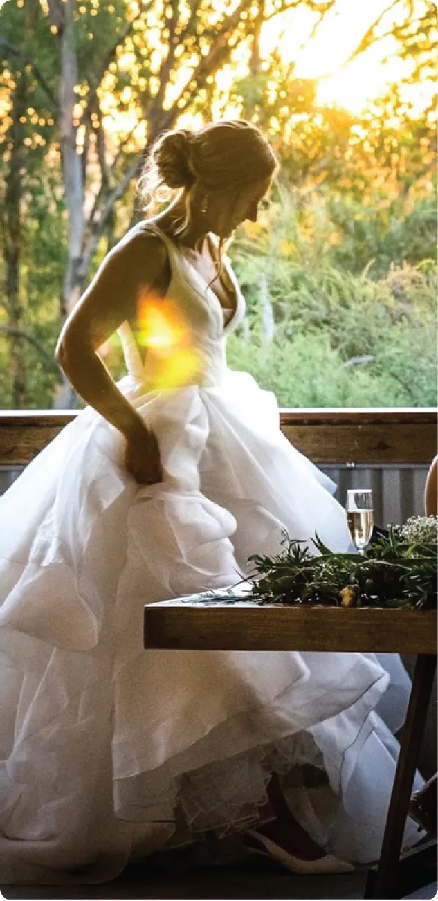 Bride Jemma in a ruffled white gown standing on a wooden balcony at sunset.