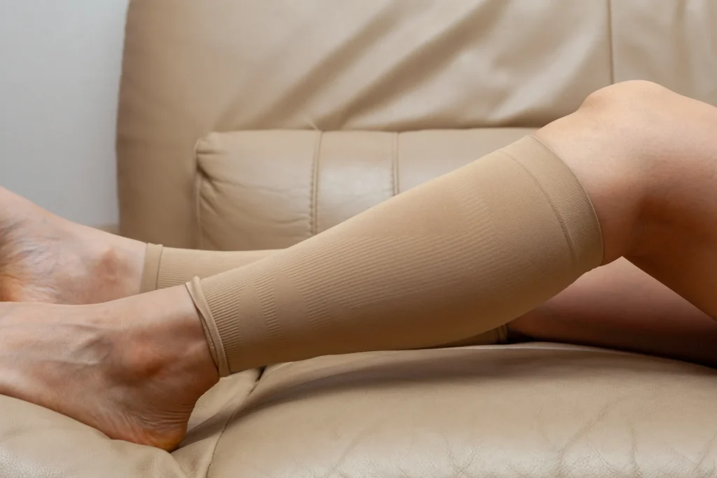 Legs in beige compression stockings resting on a tan leather sofa.