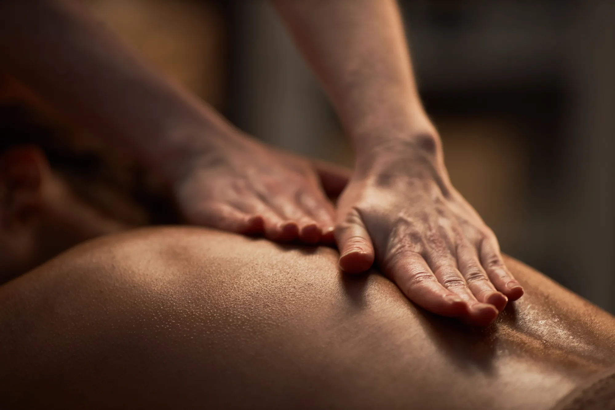 Close-up of a back massage, hands applying pressure in warm, dim light.