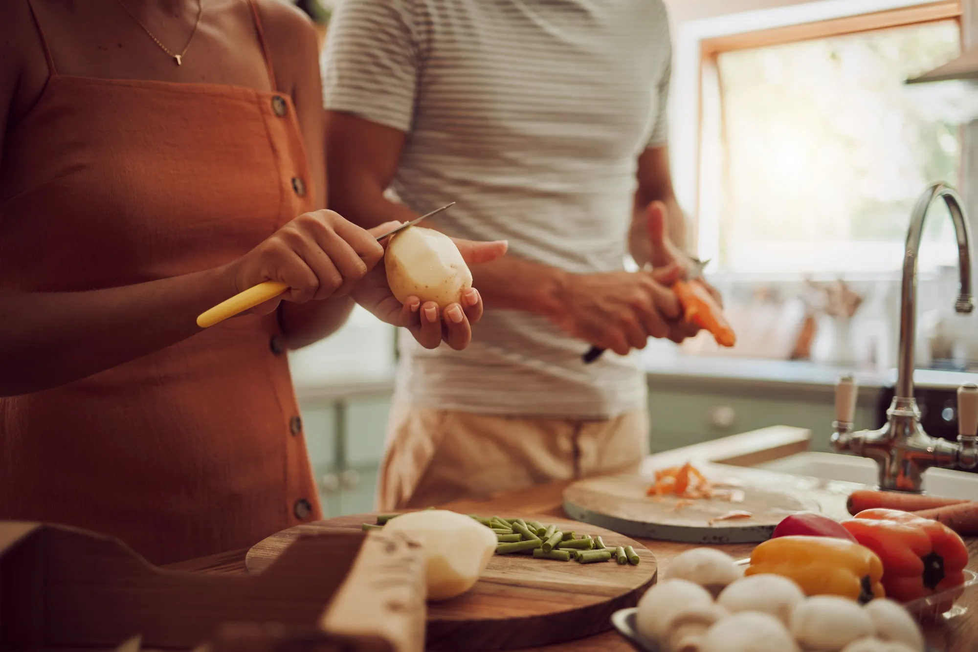 Man and woman preparing vegetables together in a sunlit kitchen.