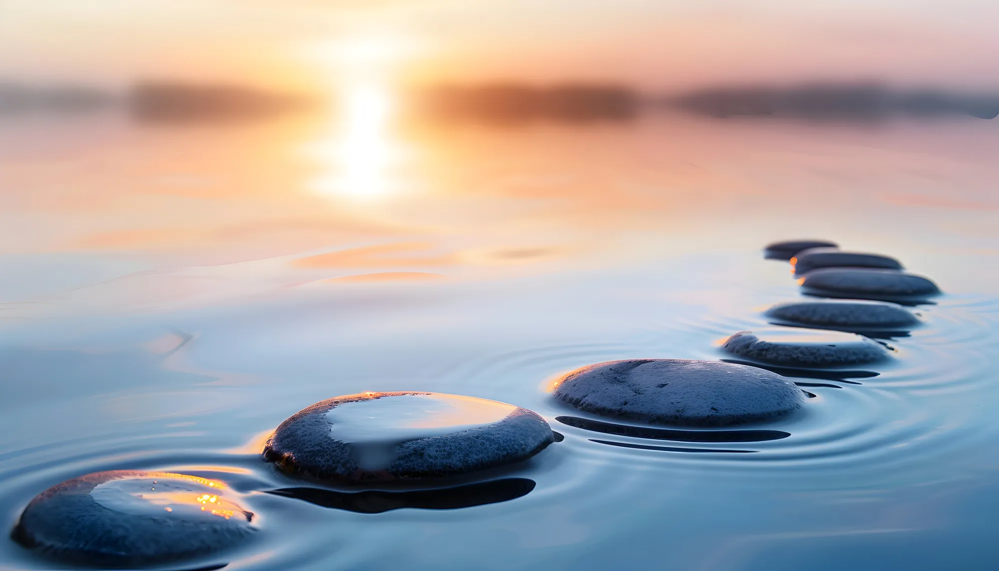 Smooth stones forming a path across calm water during a glowing orange sunset.