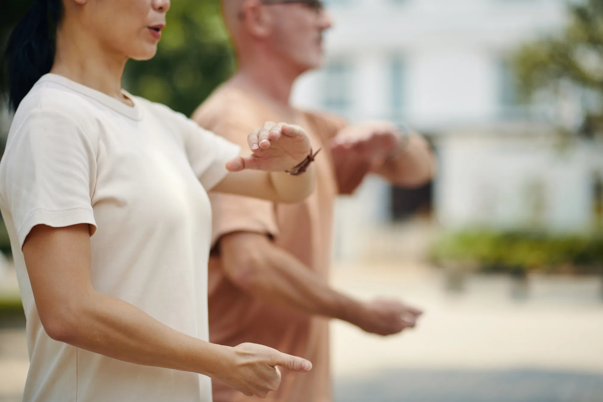 Side profile of two people practicing fluid, meditative Tai Chi in a soft-focus park.